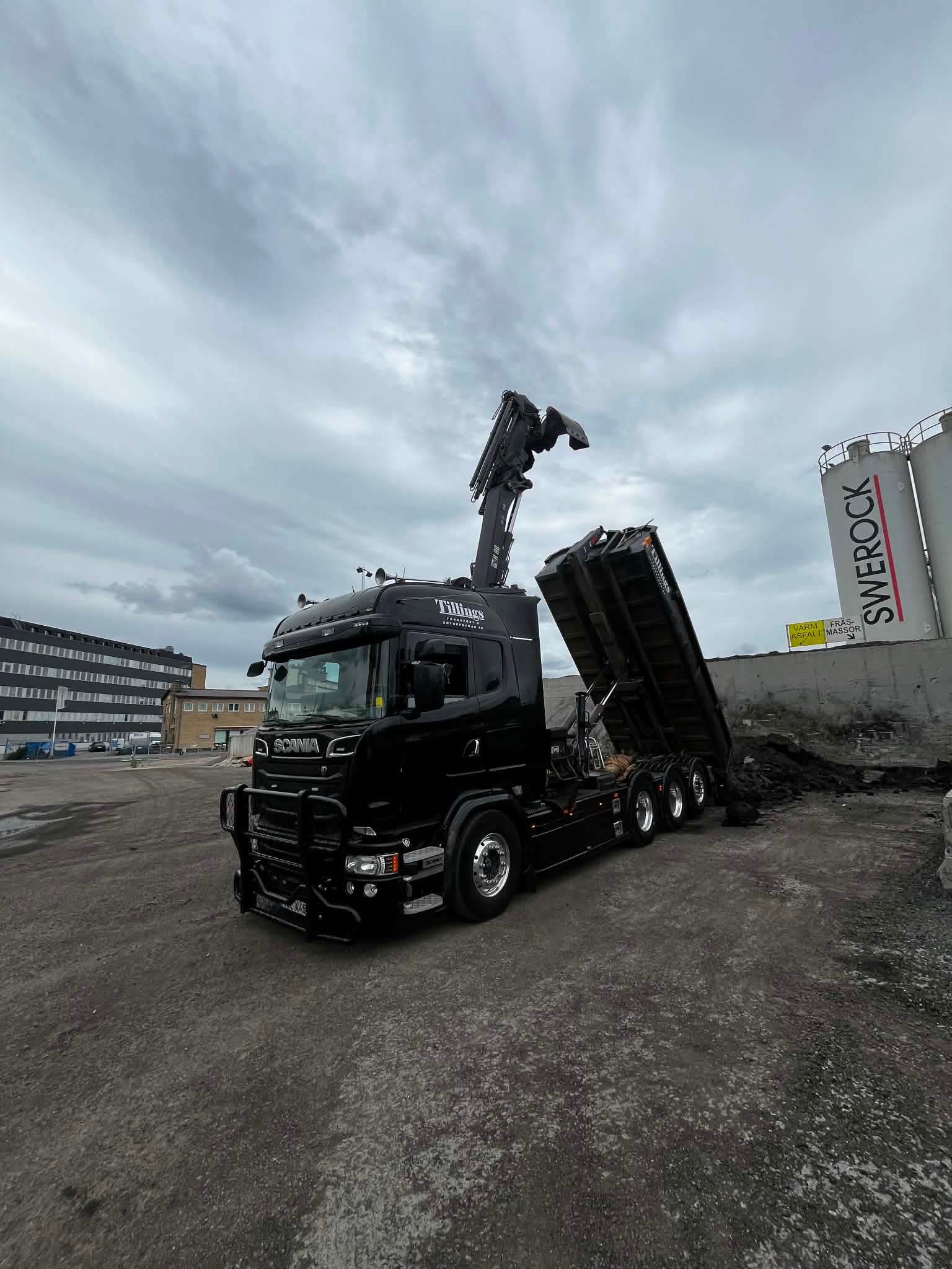 Tillings svarta Scania kranbil med kranen uppfälld och tippflaket rest