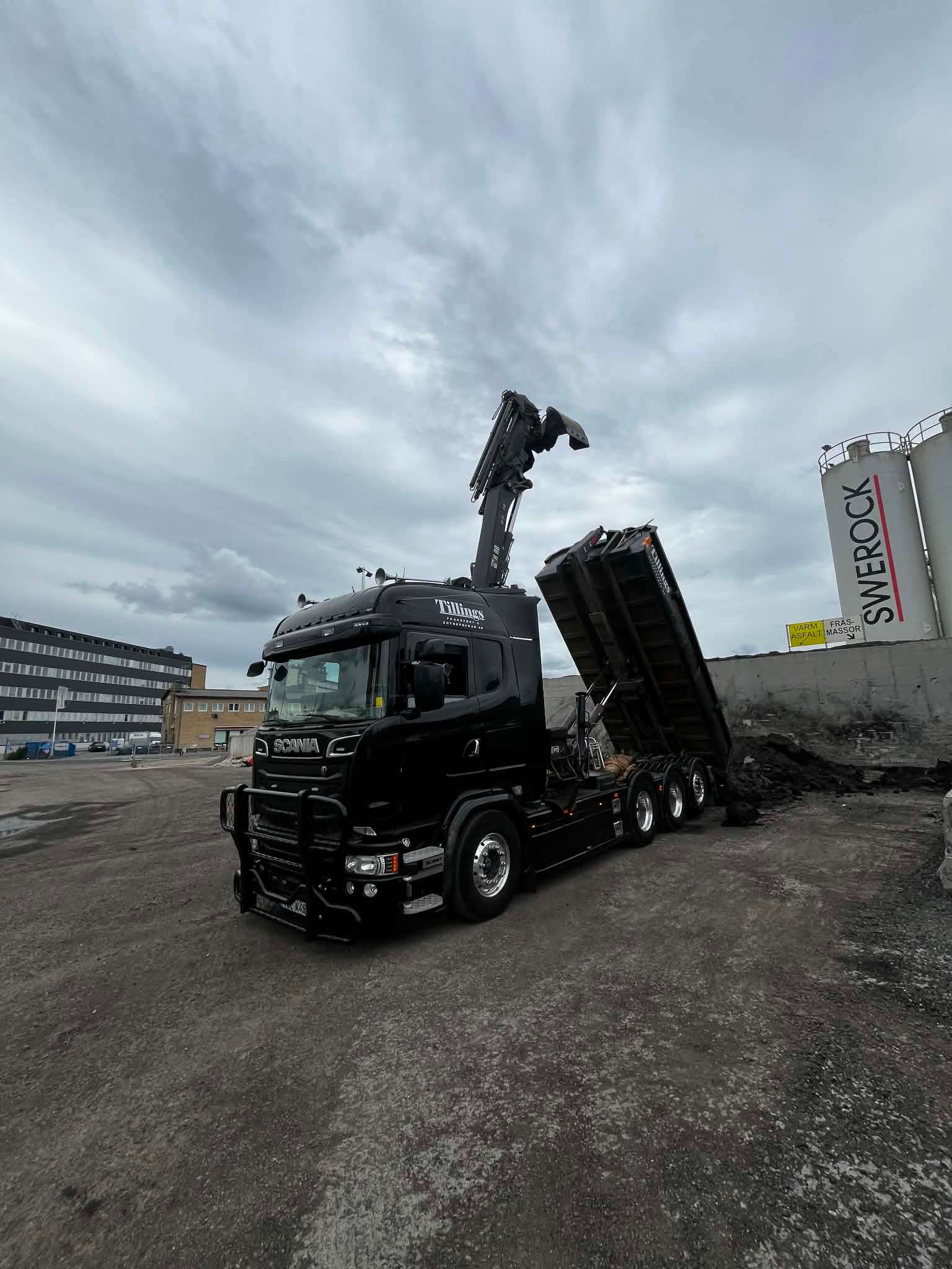 Tillings svarta Scania kranbil med kranen uppfälld och tippflaket rest