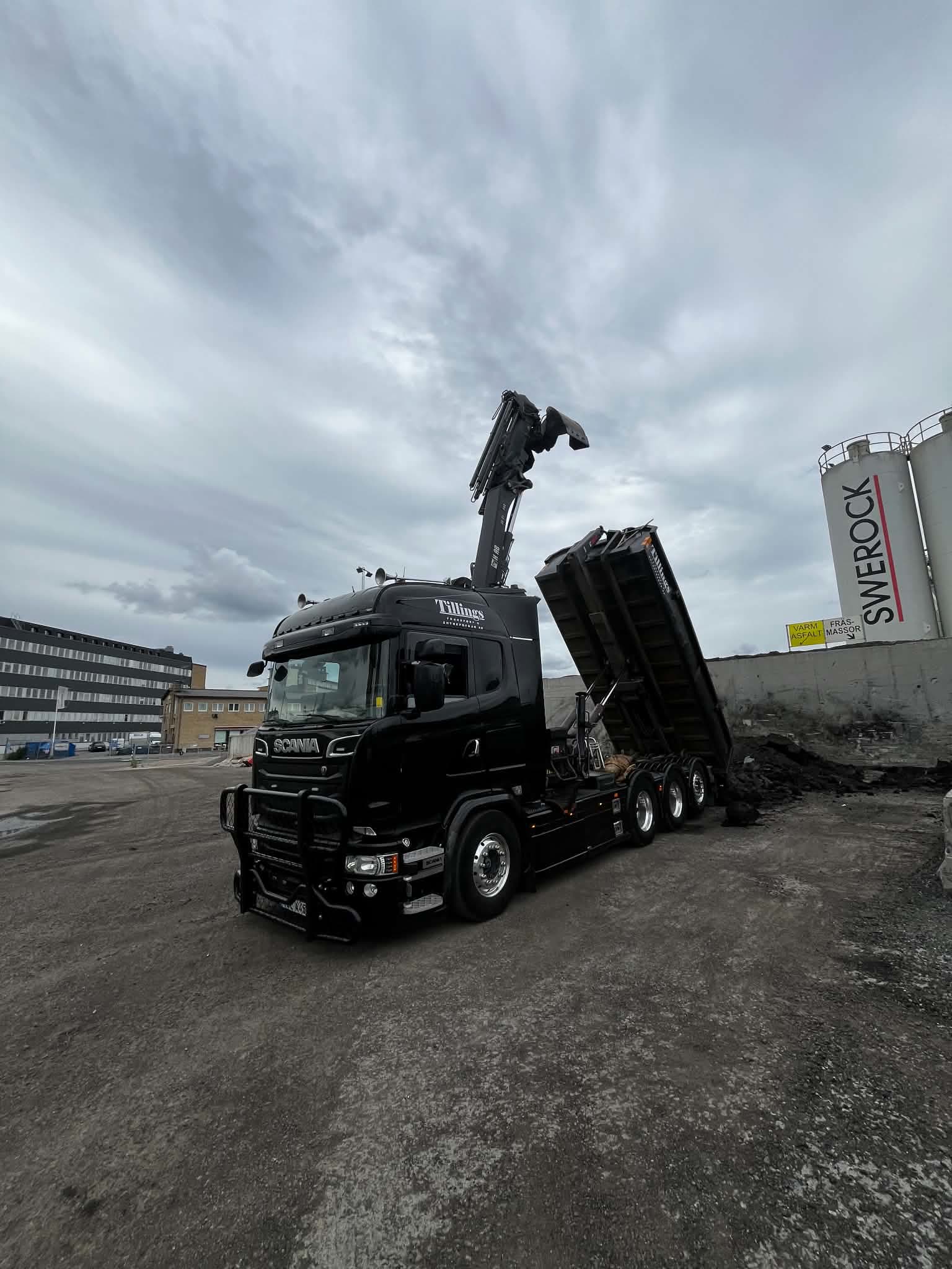Tillings svarta Scania kranbil med kranen uppfälld och tippflaket rest